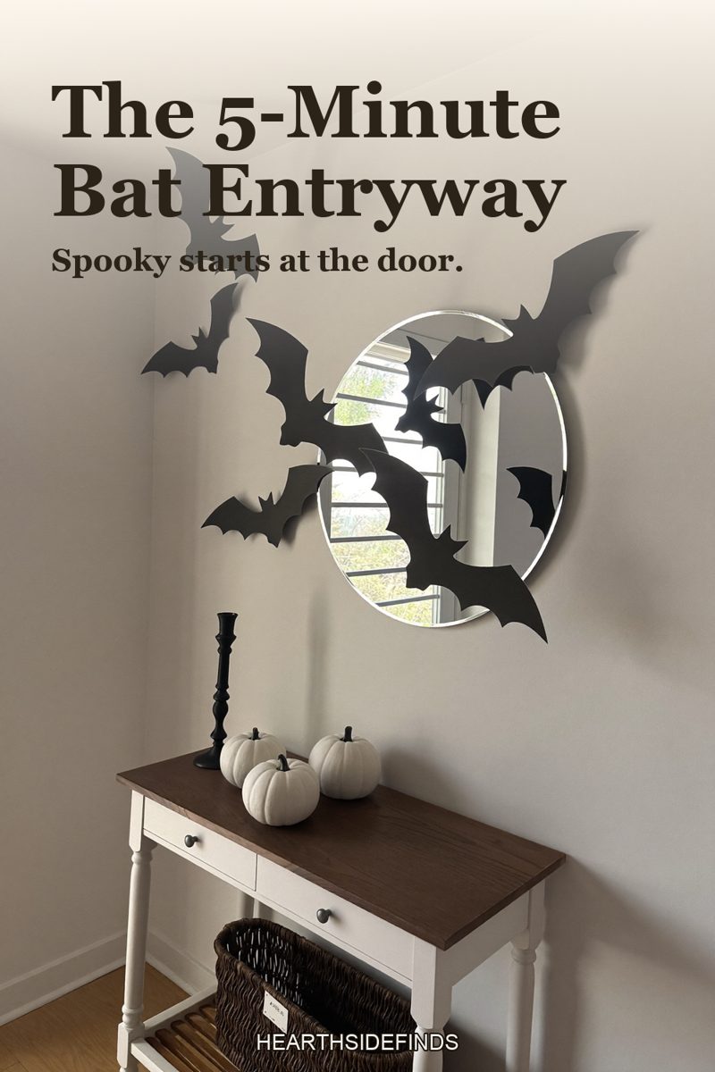 Entryway console with round mirror and white pumpkins, black paper bats fanning out across the wall from the mirror.