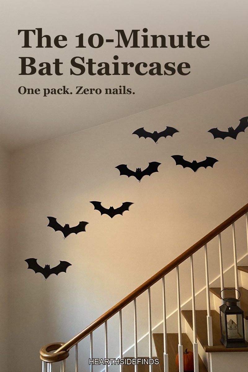 White staircase wall covered in a diagonal swarm of black paper bats, with a pumpkin and lantern on the lower steps.