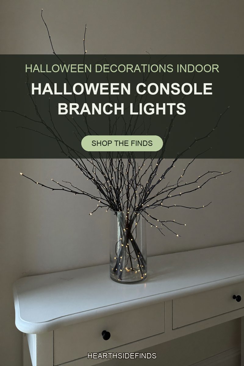 Black branches with tiny warm LED buds in a clear glass cylinder vase on a white console table.