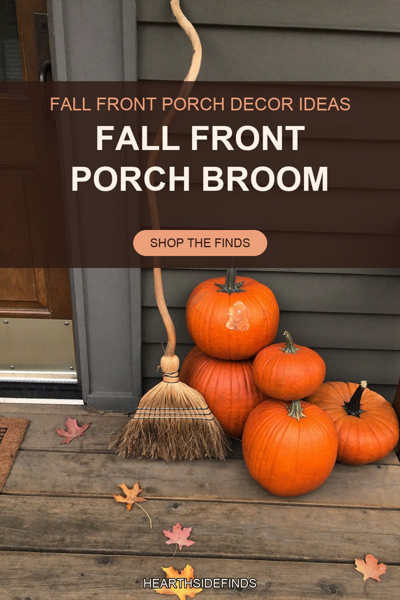 Straw broom with a twisted wooden handle leaning on gray siding beside five orange pumpkins on a wood porch.