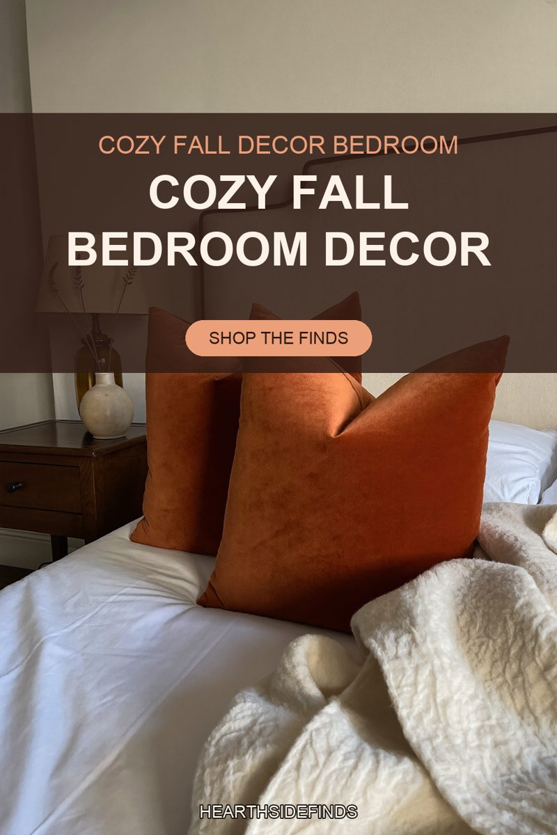 Three rust velvet throw pillows stand upright on white bedding in front of a cream upholstered headboard, the two rear pillows flanking the one in the centre, a cream textured blanket gathered across the lower right of the bed, and a dark wood nightstand at the left holding a round cream stoneware vase under a pale lamp shade.
