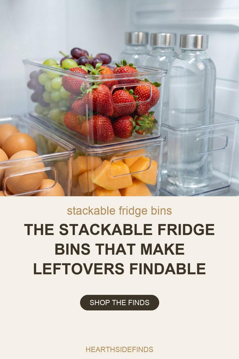Close photo inside a white refrigerator where clear handled bins are stacked two high on one shelf: the top bin holds strawberries with green and purple grapes behind them, the bin under it holds cut cantaloupe chunks, a third bin at the left edge holds brown eggs, and at the right an empty clear bin sits in front of three glass bottles of water with plain metal caps