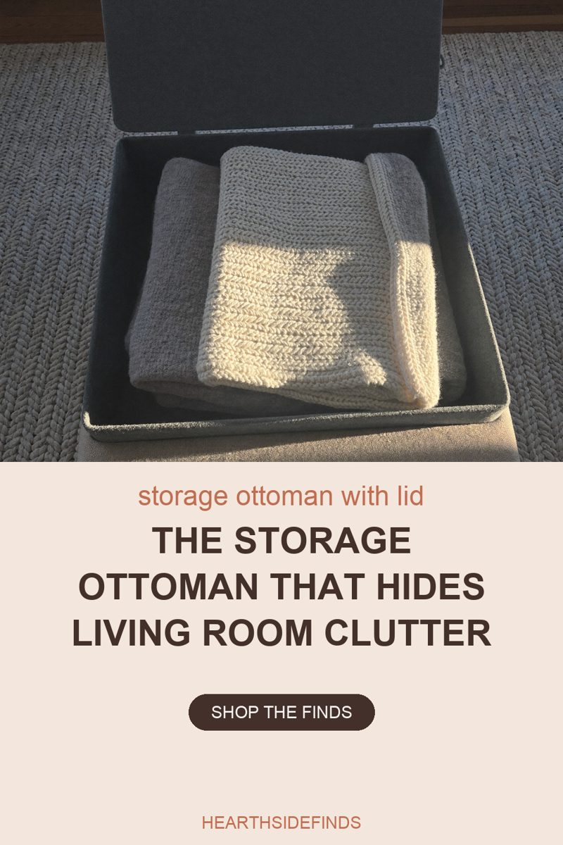 Grey upholstered storage ottoman seen from above with its lid hinged open and standing upright across the back of the frame. Inside the deep fabric-lined compartment sit two folded chunky-knit blankets, a cream one resting on a grey one, with low sunlight falling in a bright band across the cream knit. The ottoman's taupe woven side wall runs along the bottom edge, a thick grey braided rug fills the top and side margins, and a strip of dark wood floor shows in the top corners.
